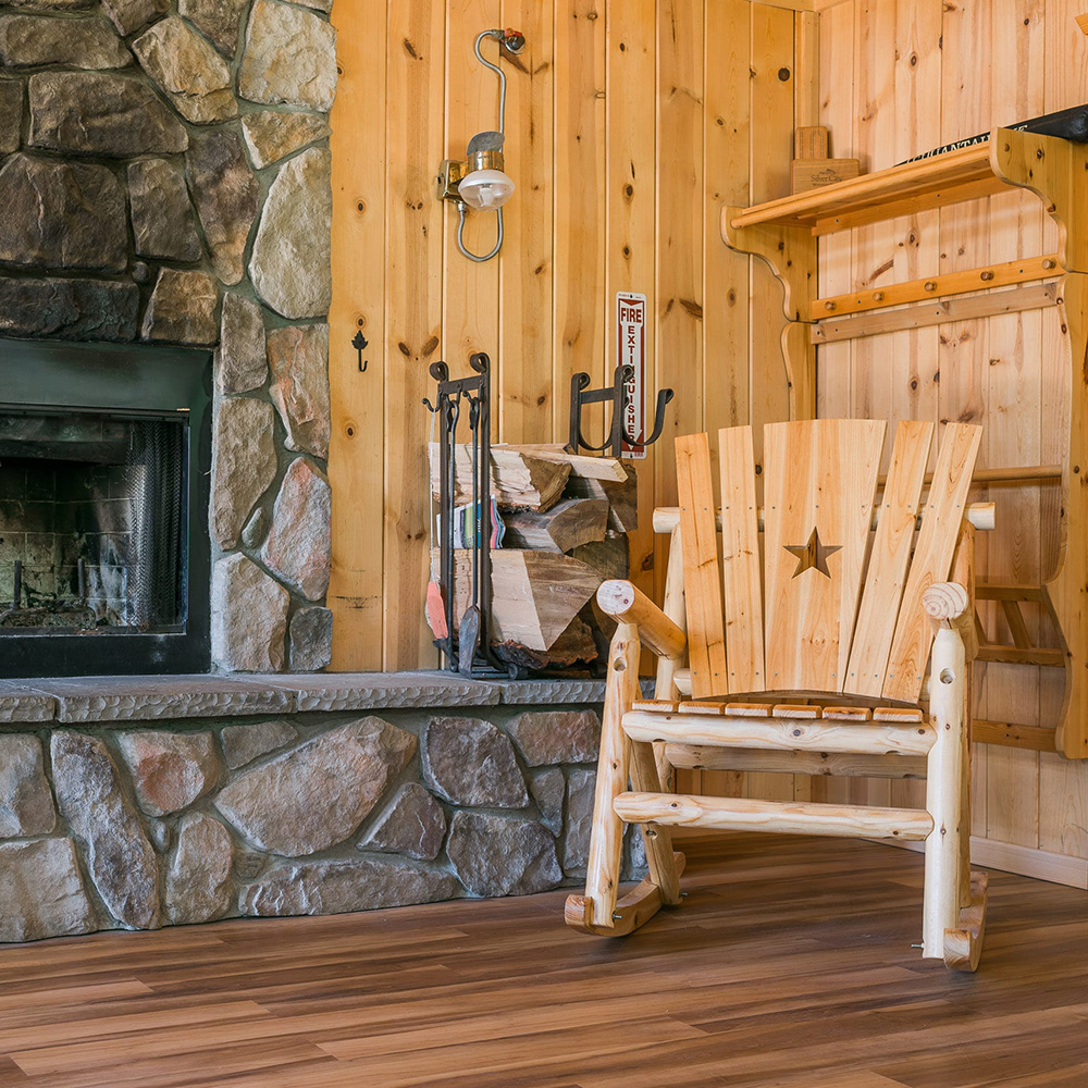 Cozy cabin interior corner showcasing a stone fireplace, a rack of chopped firewood, and a rustic wooden rocking chair with a star cut-out design on the backrest.