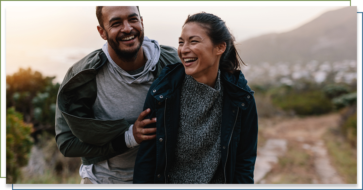 Man and a woman in nature, smiling.